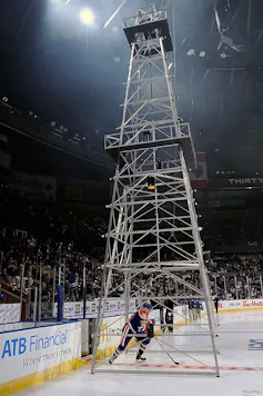 A man in hockey gear skates underneath a metal scaffold meant to look like oil machinery.