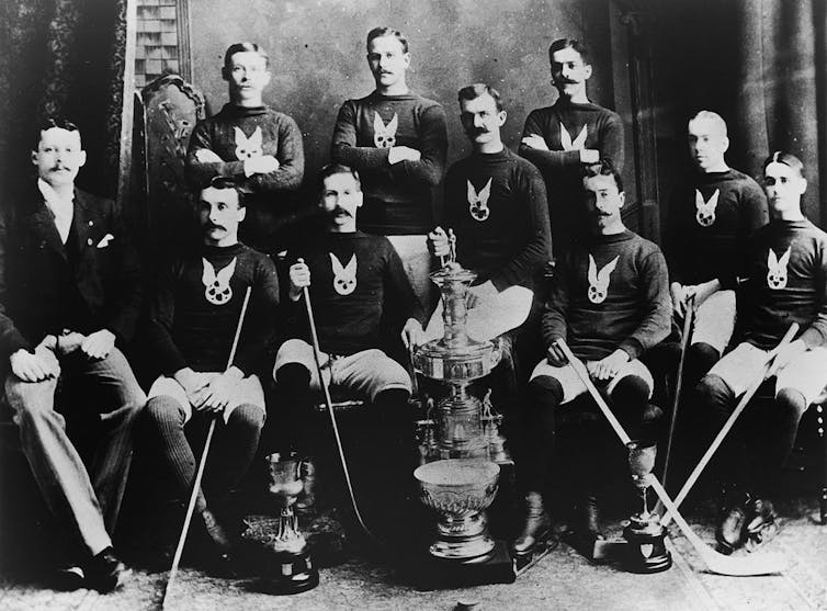 A black and white photograph of two rows of men in matching sweaters posing formally with hockey sticks.