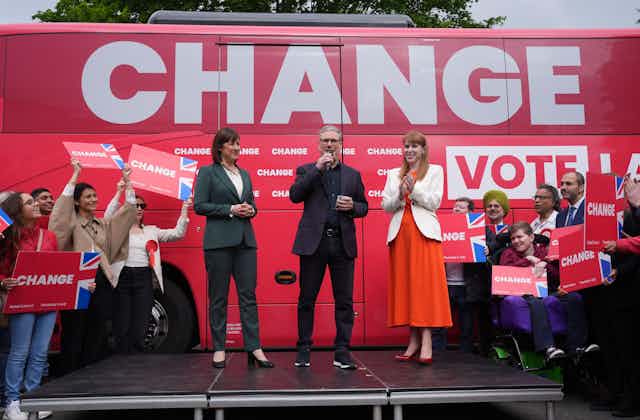 Rachel Reeves, Keir Starmer and Angela Rayner standing on a stage in front of a bus with the word 'change' printed in huge letters on its side.