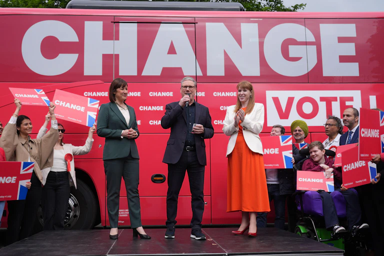 Rachel Reeves, Keir Starmer and Angela Rayner standing on a stage in front of a bus with the word 'change' printed in huge letters on its side.