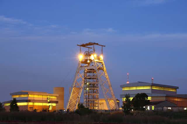Tower-like structure and buildings, lit up against an evening sky