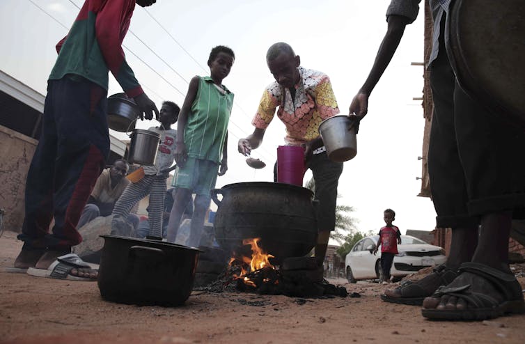 People tend to food in a large iron pot over an open flame.