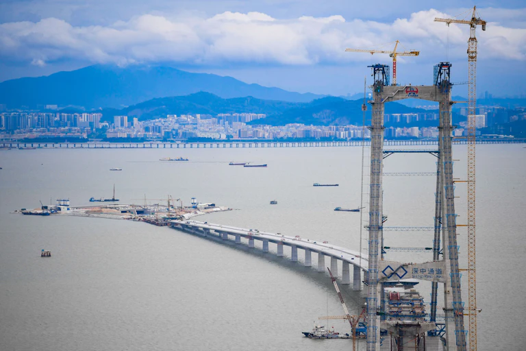 scaffolding and boats around a partially constructed bridge with shoreline in background