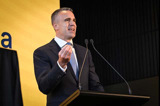 A man in a suit gives a speech behind a lectern