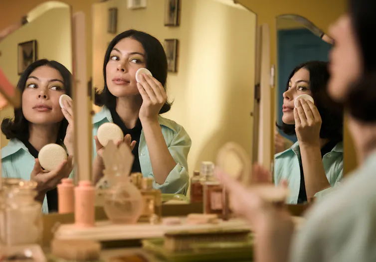 Production still: a woman puts on make-up