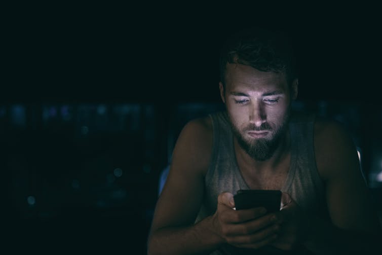 A man looks at a mobile phone in the dark.