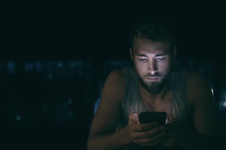 homem olha para o celular em um ambiente escuro
