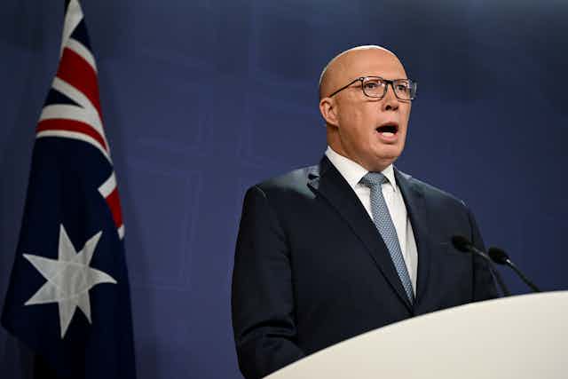 man stands at podium in front of Australian flag