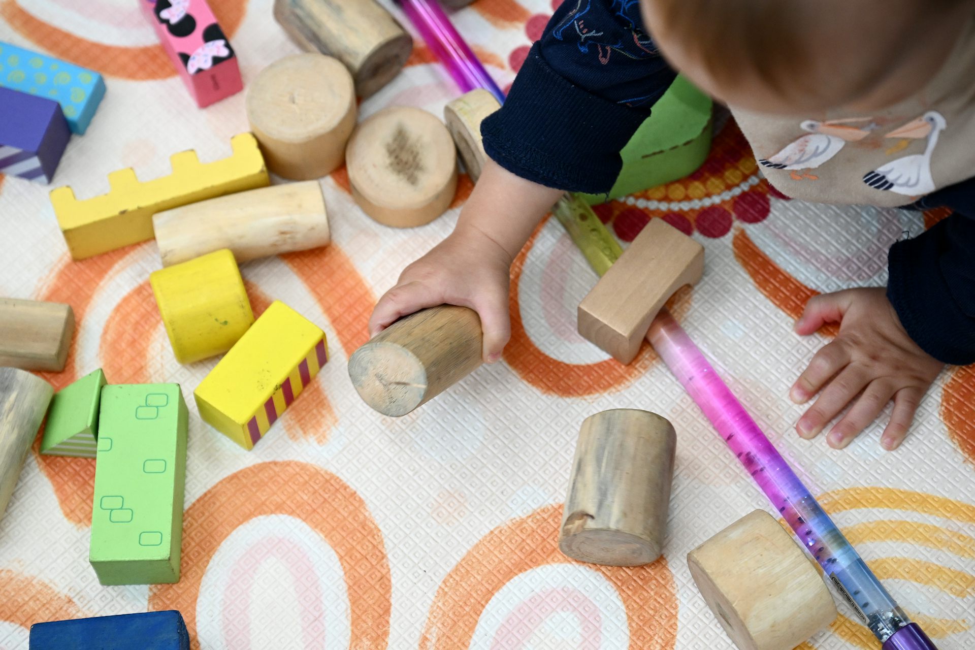 An infant plays with wooden blocks on a mat.