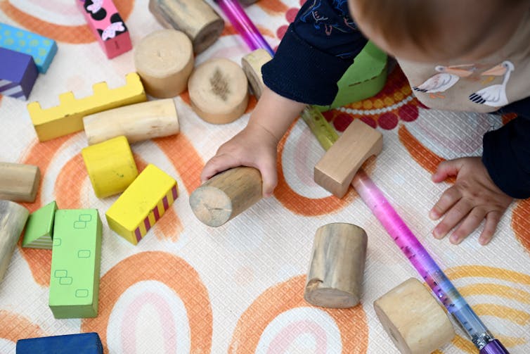 An infant plays with wooden blocks on a mat.