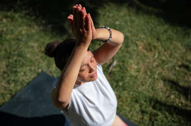 woman on yoga mat outdoors sits with eyes closed