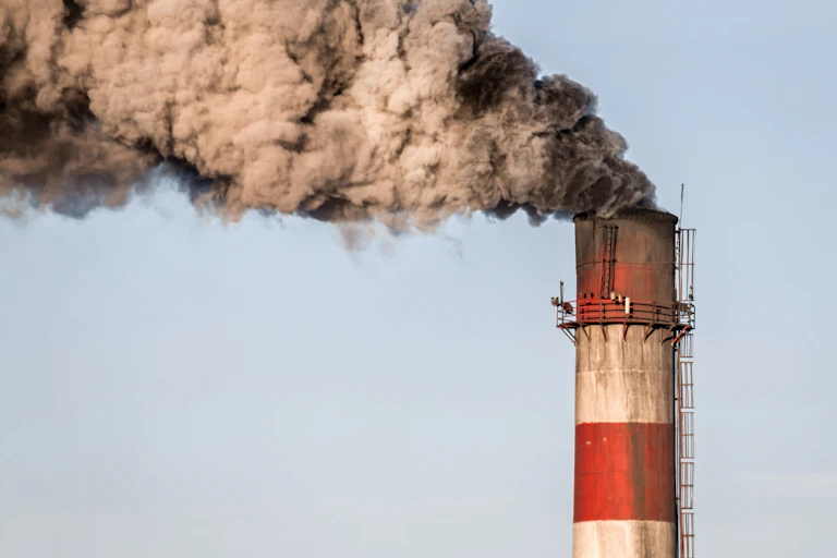 A red and white industrial chimney spewing black smoke.
