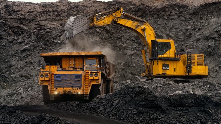 An excavator piles coal onto a truck.