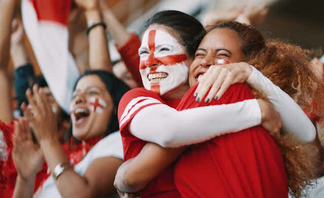 Two women football fans hugging, one with the St George cross painted on her face.