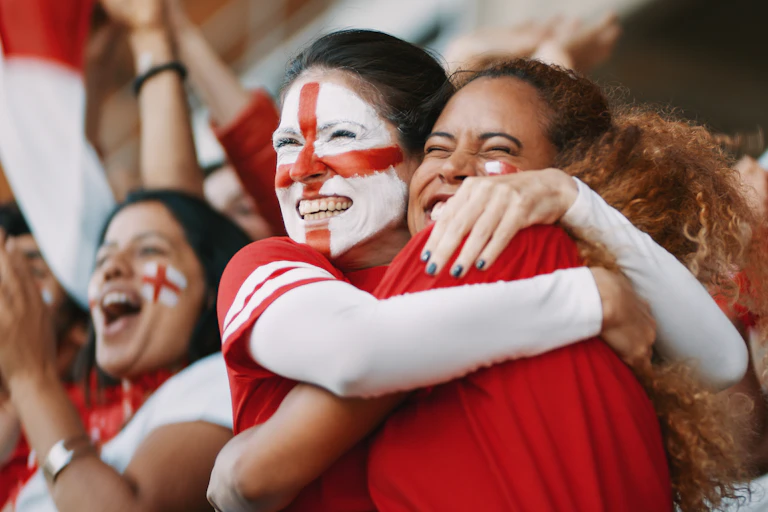Two women football fans hugging, one with the St George cross painted on her face.