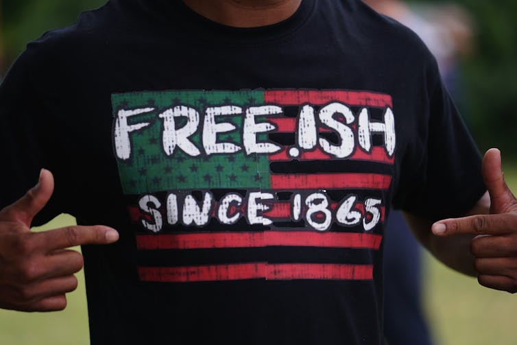 A black man wears a T-shirt that says “Freeish since 1865.”