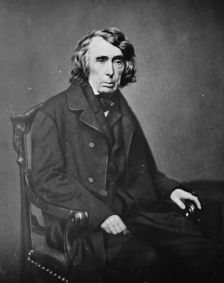 A white man wearing a black robe poses for a portrait.