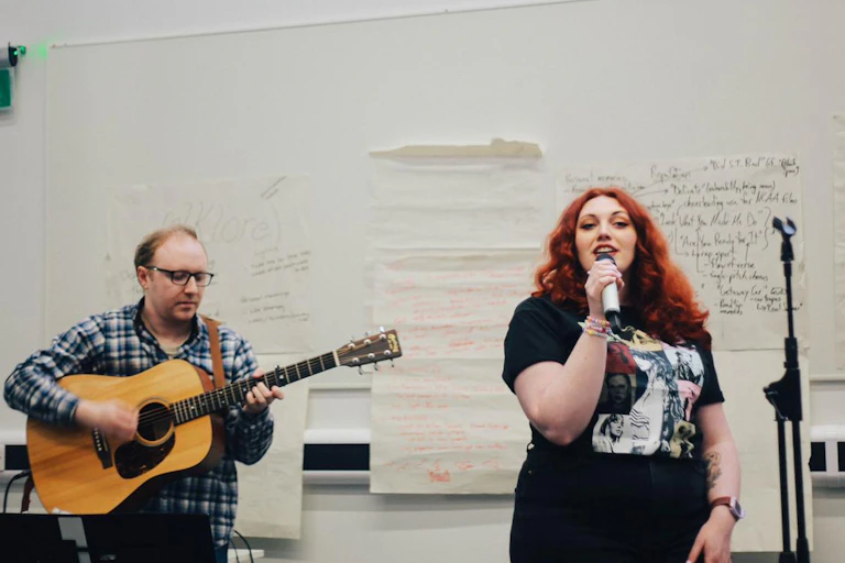 A singer with red hair next to a man playing acoustic guitar.