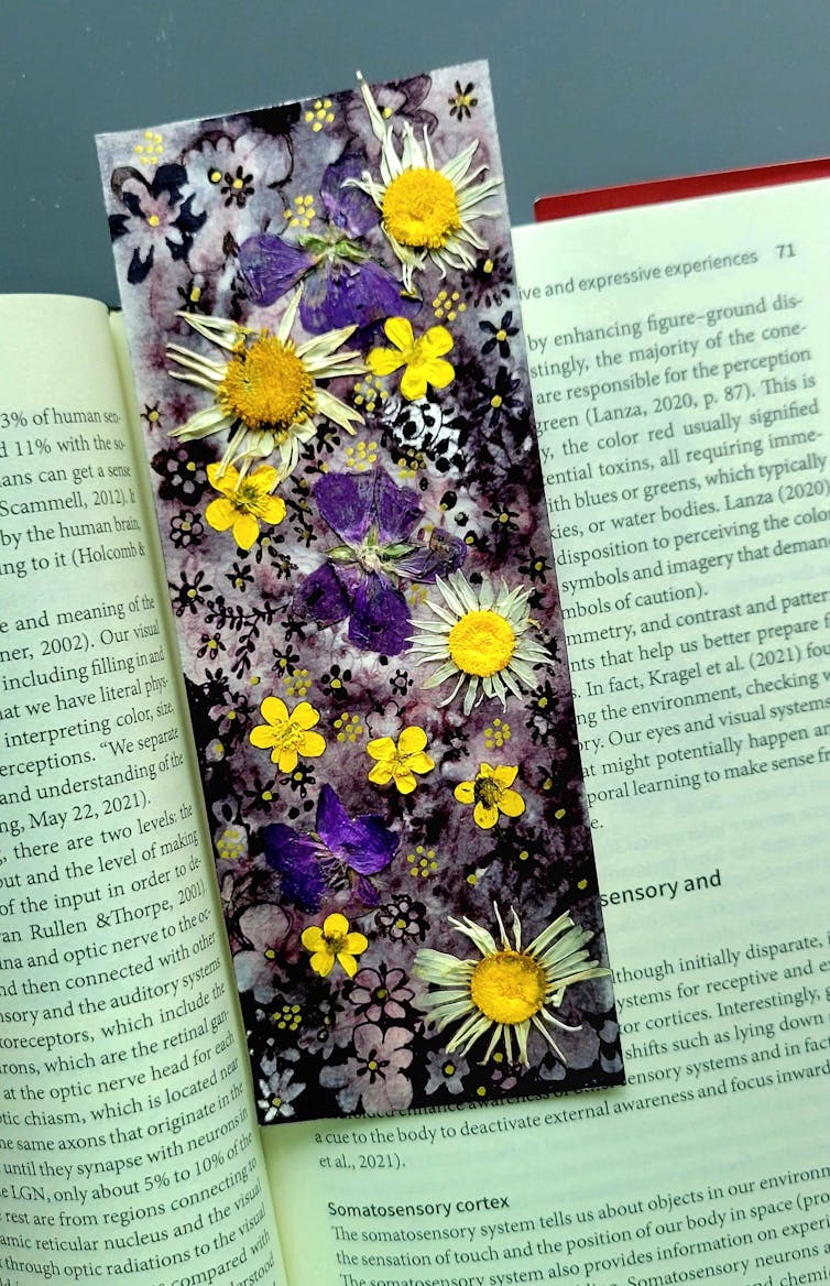 A bookmark covered in purple, white and yellow flowers sits on an open book.