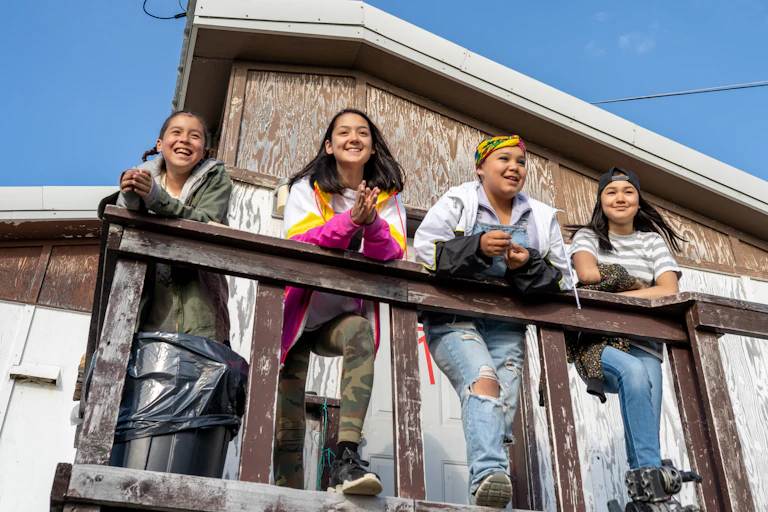 Girls standing on a porch surveying space and smiling.
