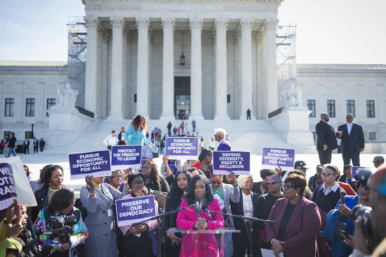 Black women gathered in front of a building with columns, holding signs calling for opportunities for all.