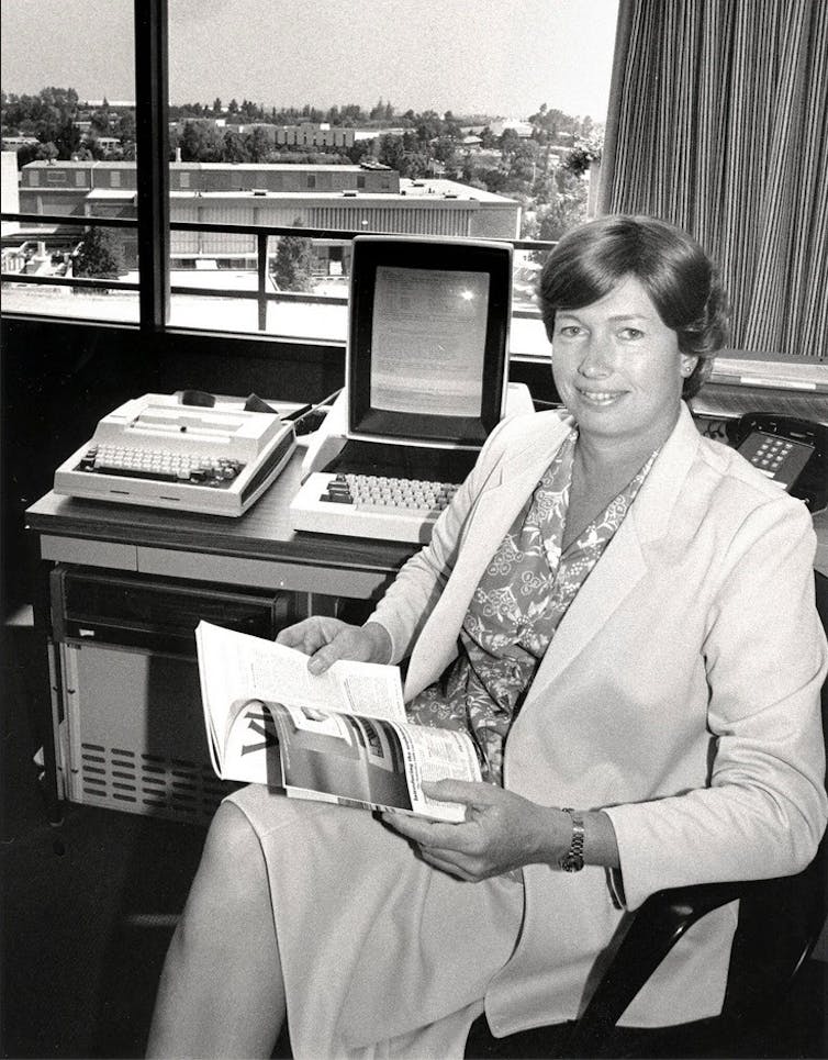 black and white photo of a woman in business attires seated with her back to her desk