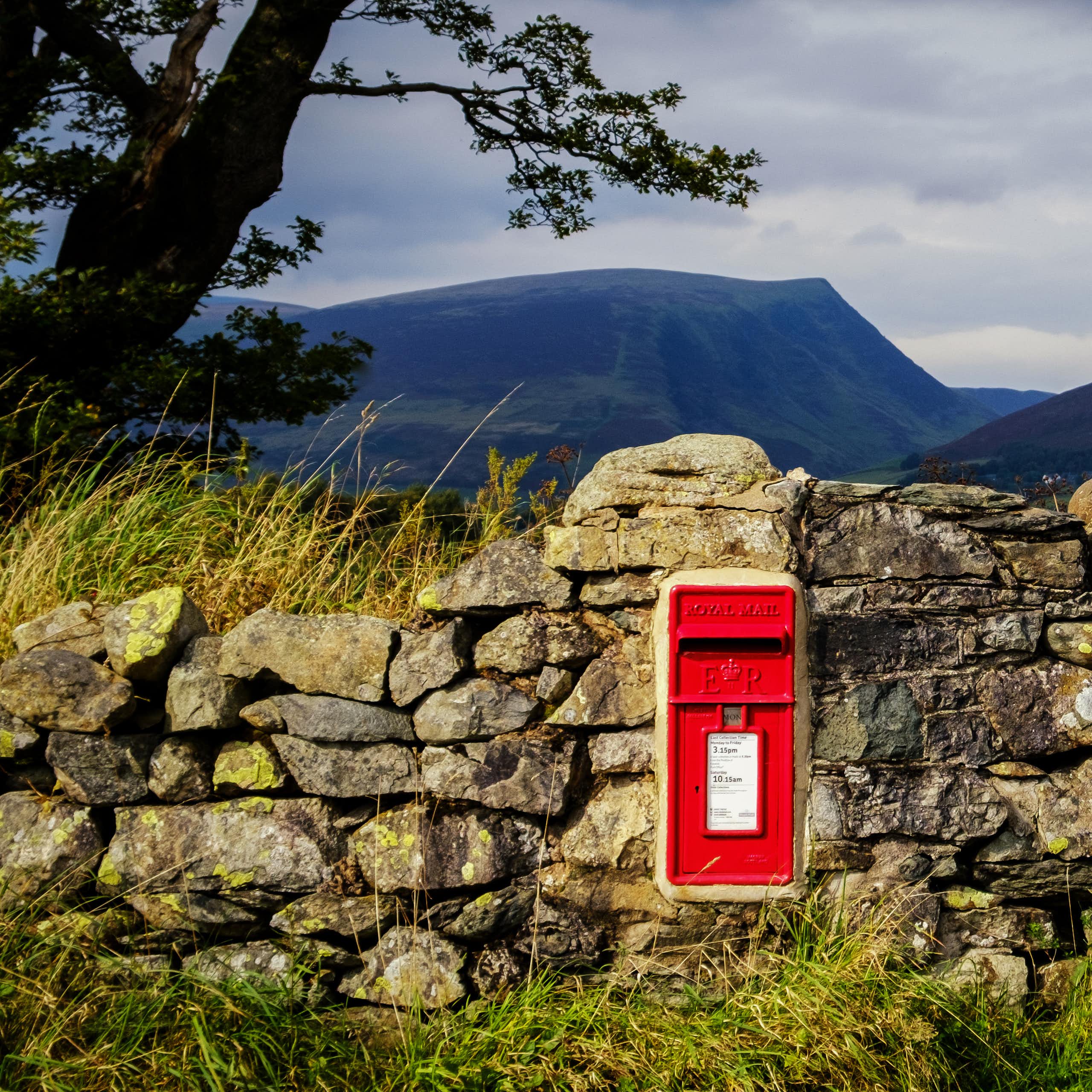 Post box in stone wall with rural backdrop.