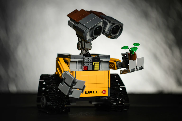 Figurine en Lego du robot WallE de Disney, regardant une petite plante qu'il tient dans sa main articulé.