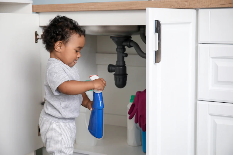 Un jeune enfant joue avec des produits nettoyants présents sous un évier.