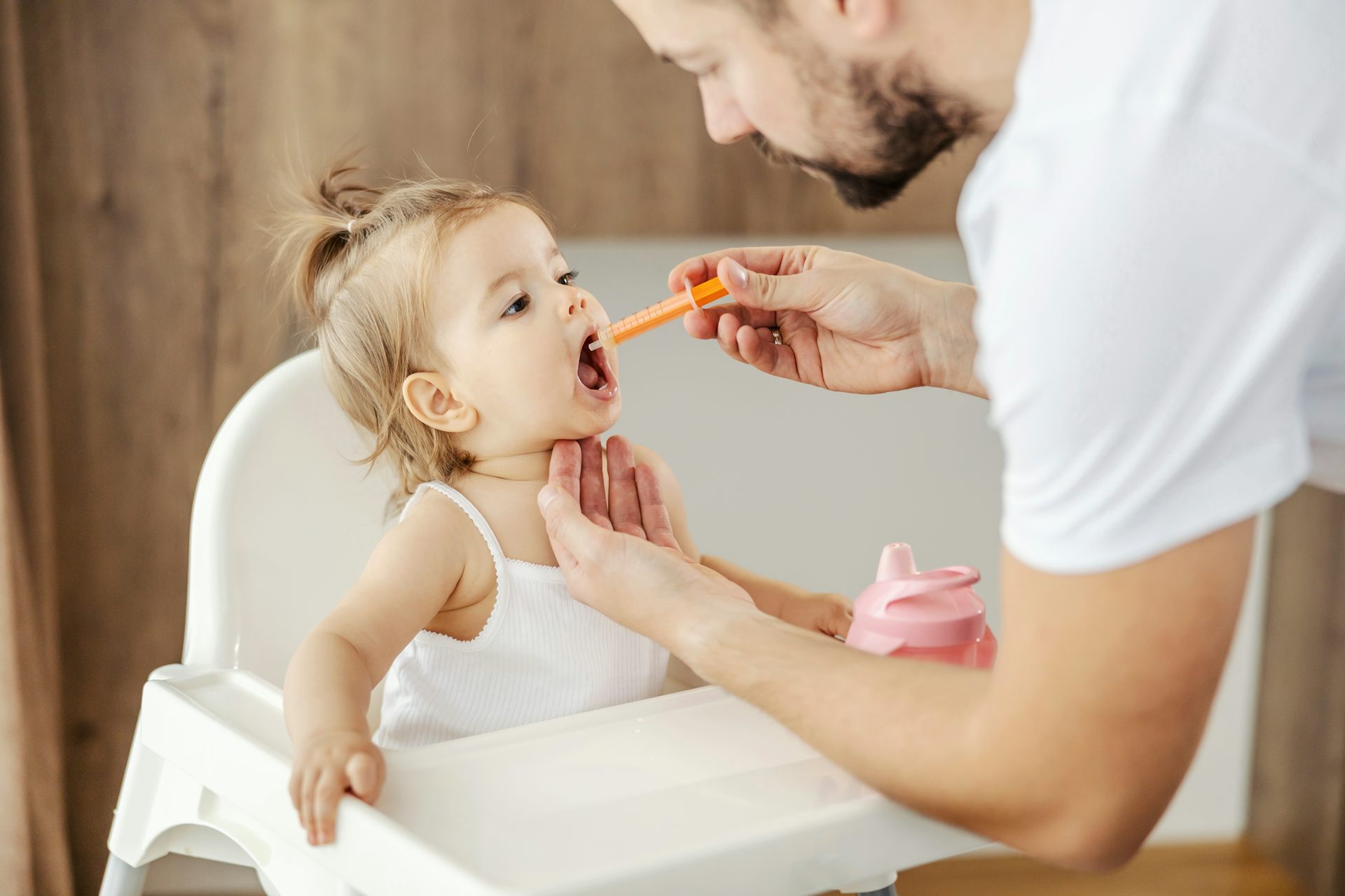 Un papa administre à la pipette un médicament à sa fille installée dans une chaise haute