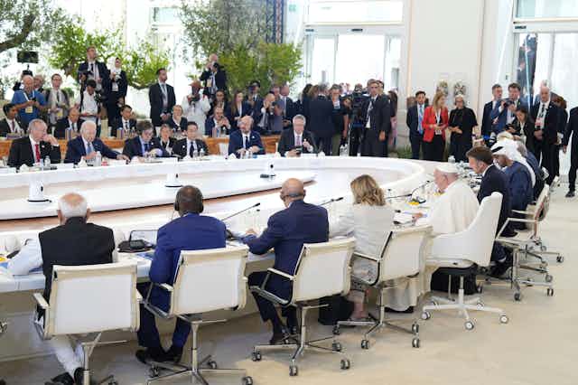 A group of leaders from G7 countries and other states sit around a big table with Pope Francis I