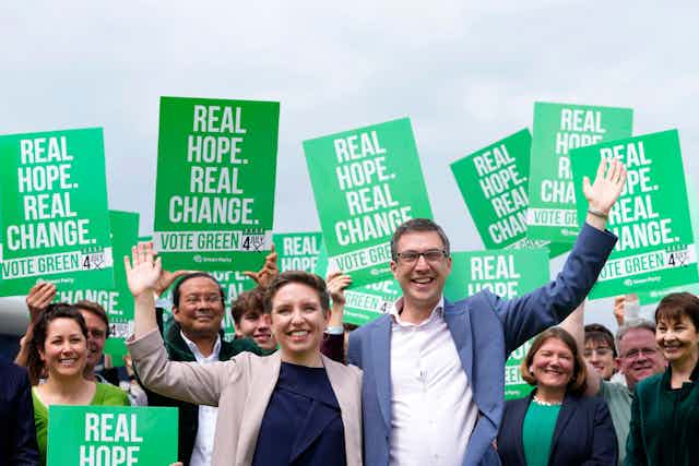 woman and man in suits with arms raised in front of supporters all holding bright green signs stating real hope, real change