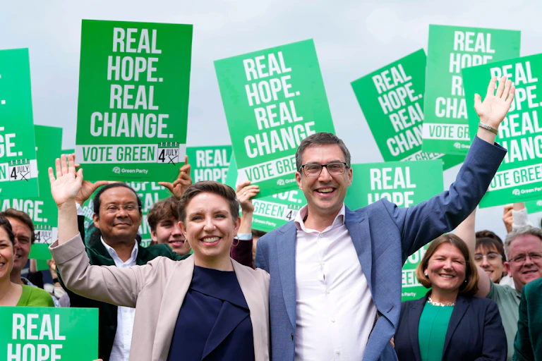 woman and man in suits with arms raised in front of supporters all holding bright green signs stating real hope, real change