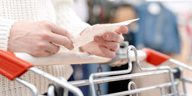 Woman's hands holding receipt over shopping trolley