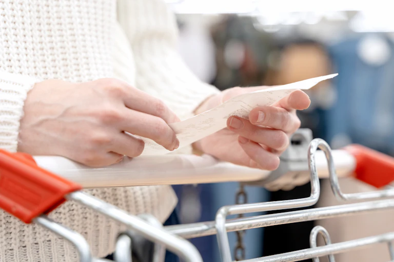 Woman's hands holding receipt over shopping trolley