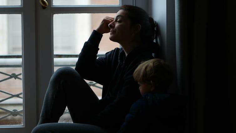 Woman looking worried and tired sat by window with toddler