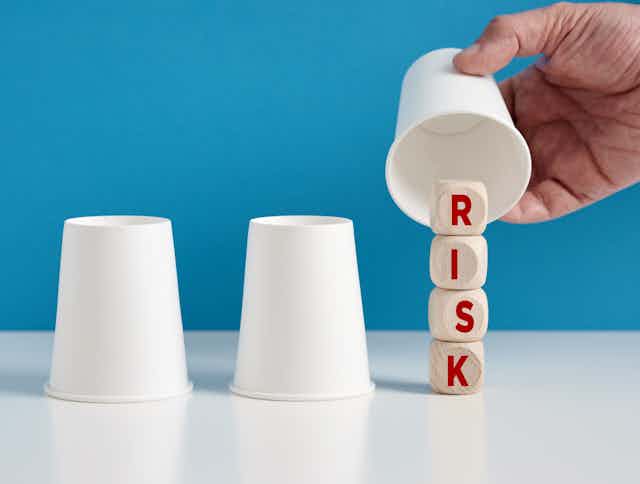 trois gobelets dont un soulevé avec des dés sur lesquels est écrit "risk"