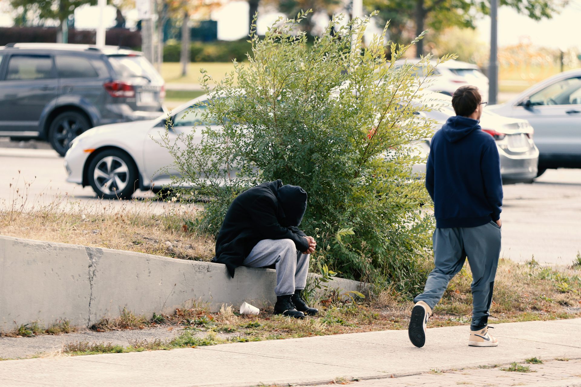 Un homme passe devant une personne recroquevillée sur le trottoir.