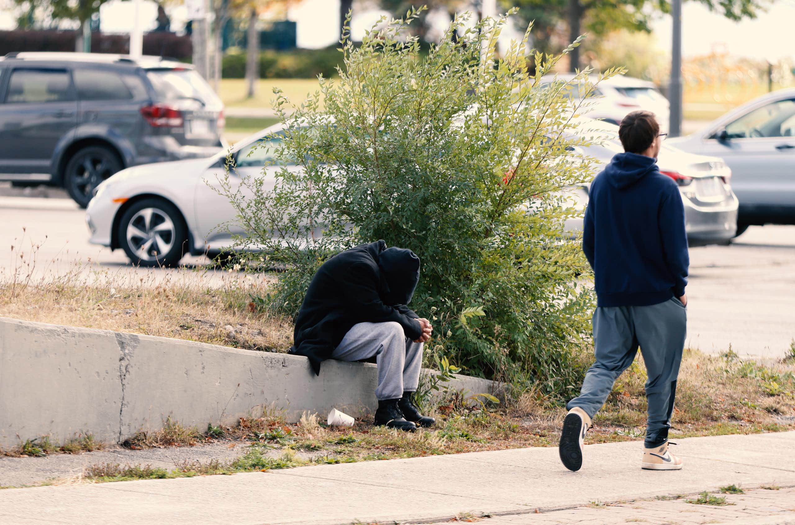 Un homme passe devant une personne recroquevillée sur le trottoir.