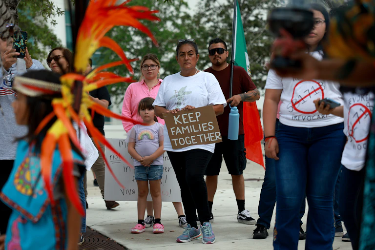A group of people stand together and a woman holds a sign that says 'Keep families together.'