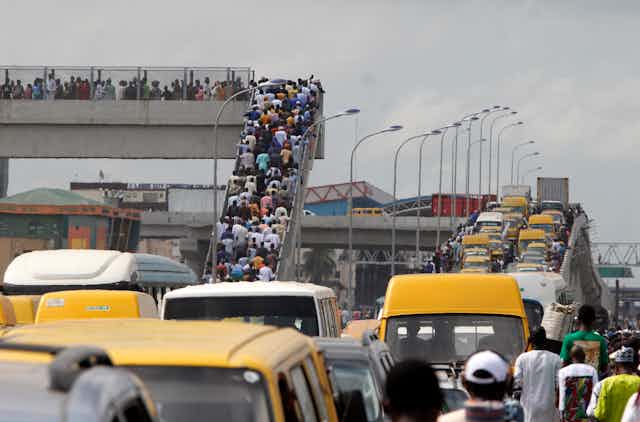 Large number of people climbing a pedesterian bridge besides a congested road