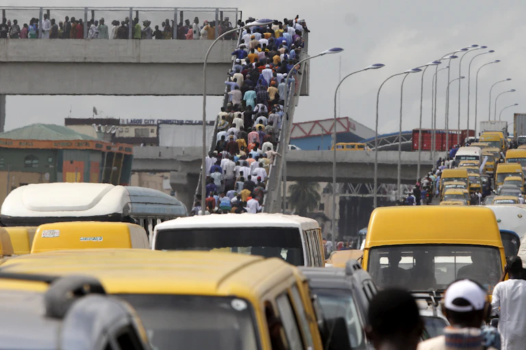Large number of people climbing a pedesterian bridge besides a congested road