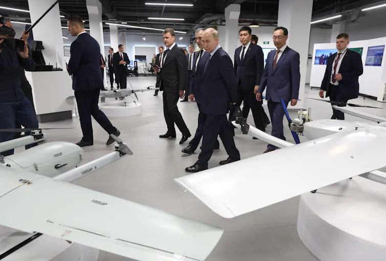 Russian president Vladimir Putin with his entourage walks around a factory making drones.