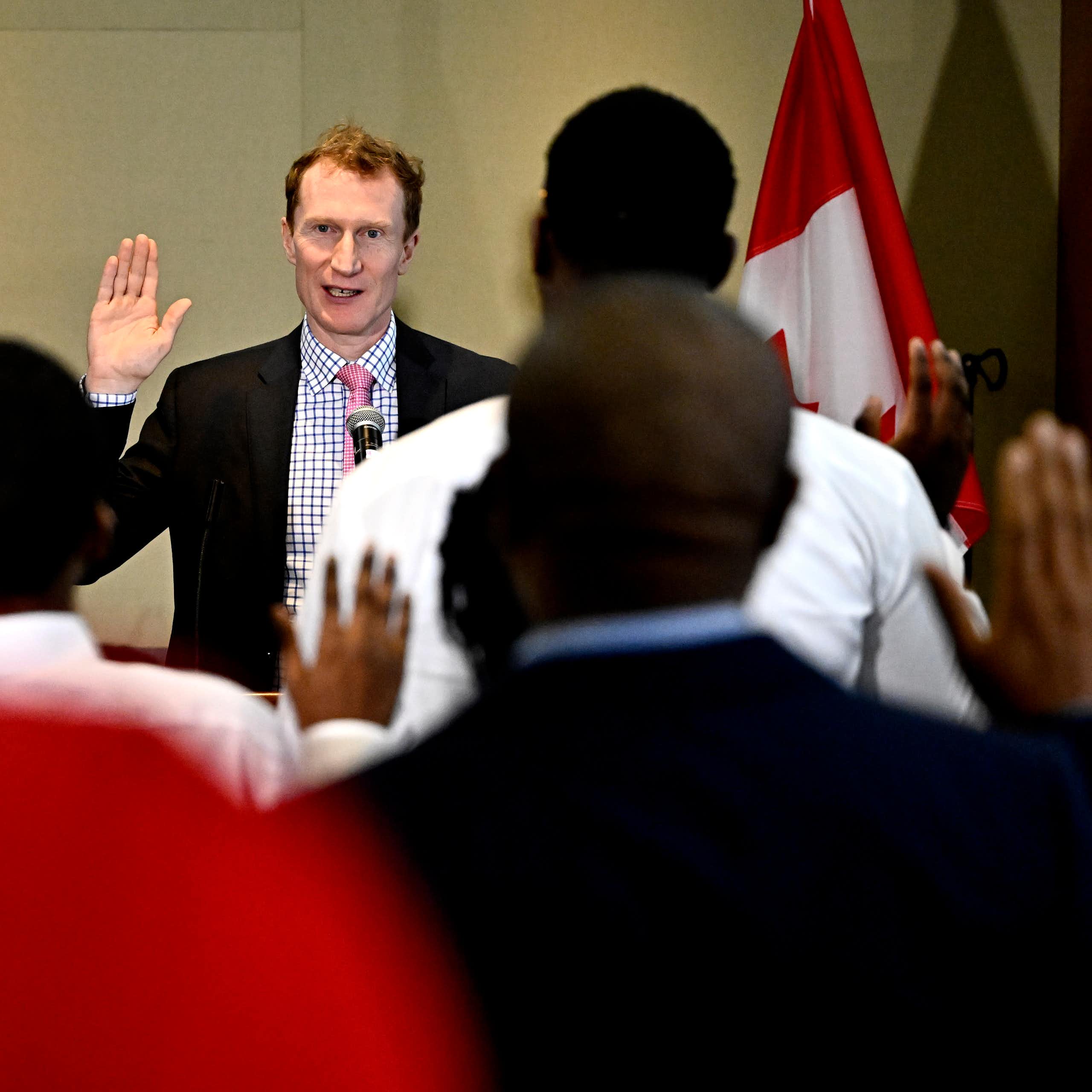 A man with red hair raises his hand as racialized people are photographed from behind raising their hands.