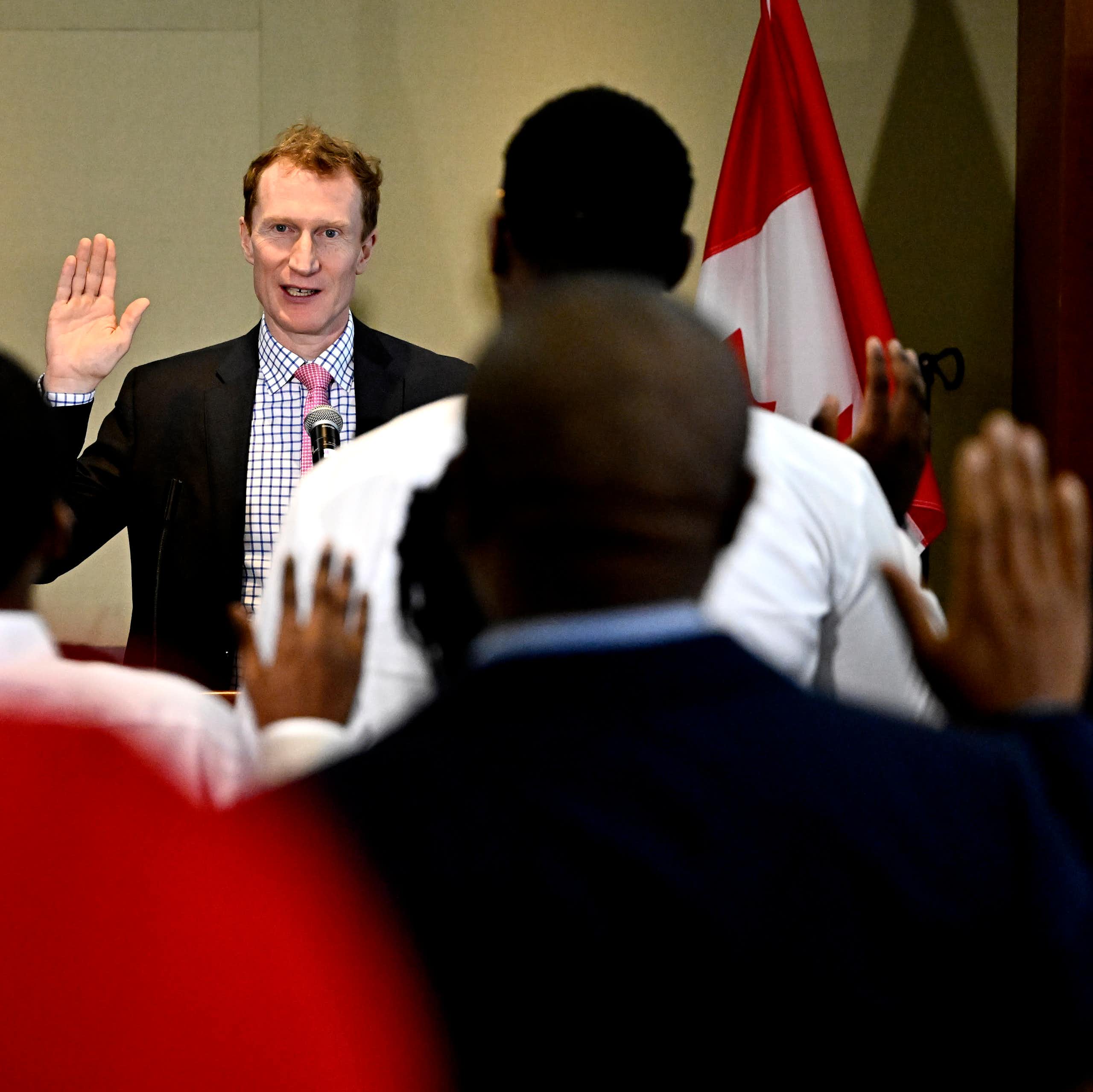 A man with red hair raises his hand as racialized people are photographed from behind raising their hands.