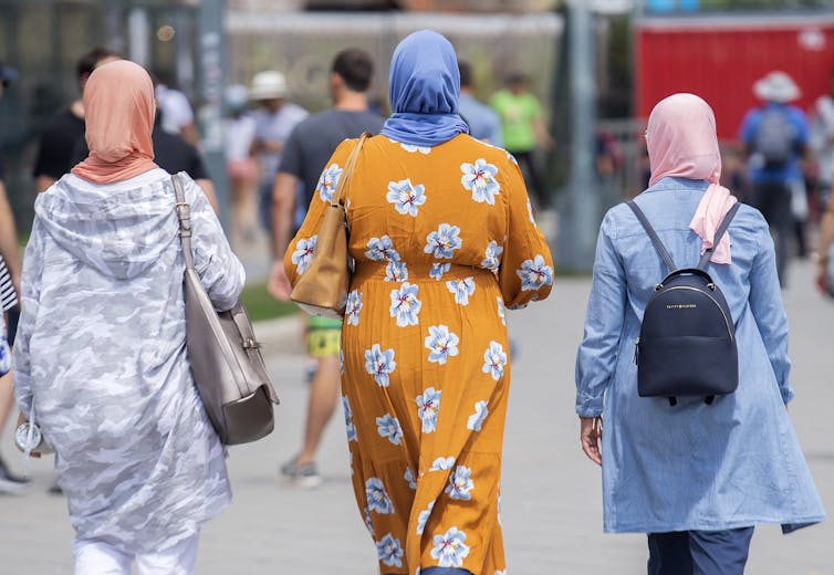 Women wearing hijabs walk together in a city setting.