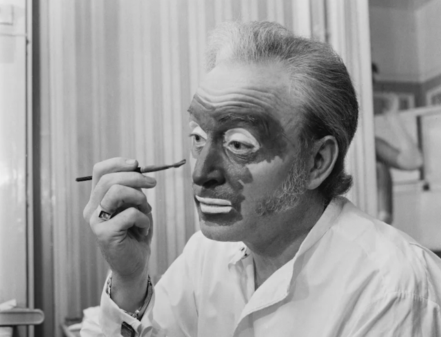 Black and white photo of white man applying dark paint to his face with a brush.Foto em preto e branco de um homem branco aplicando tinta escura em seu rosto com um pincel.