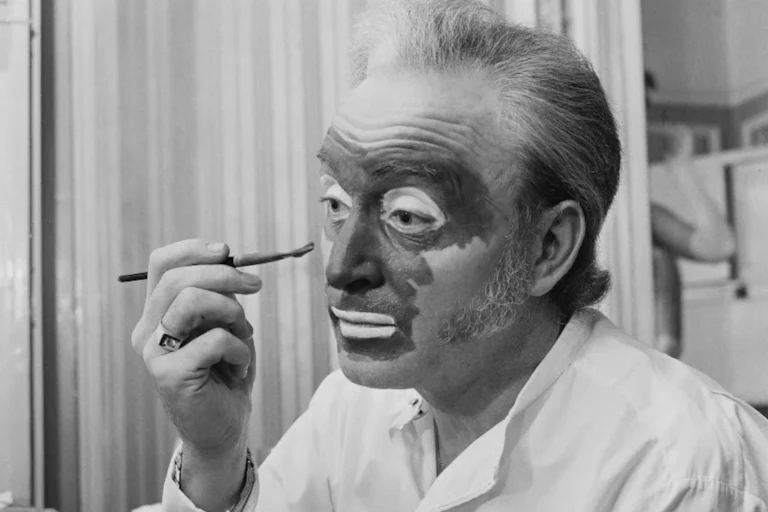 Black and white photo of white man applying dark paint to his face with a brush.Foto em preto e branco de um homem branco aplicando tinta escura em seu rosto com um pincel.