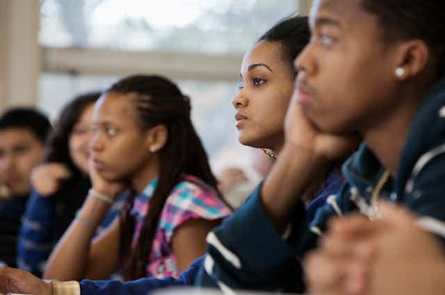 Five high school age students sit in a classroom listening