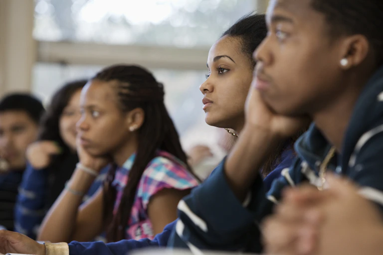 Five high school age students sit in a classroom listening